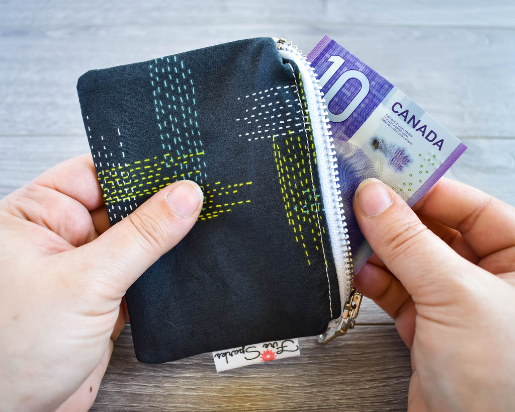 Hands removing a ten dollar bill from a dark grey change purse