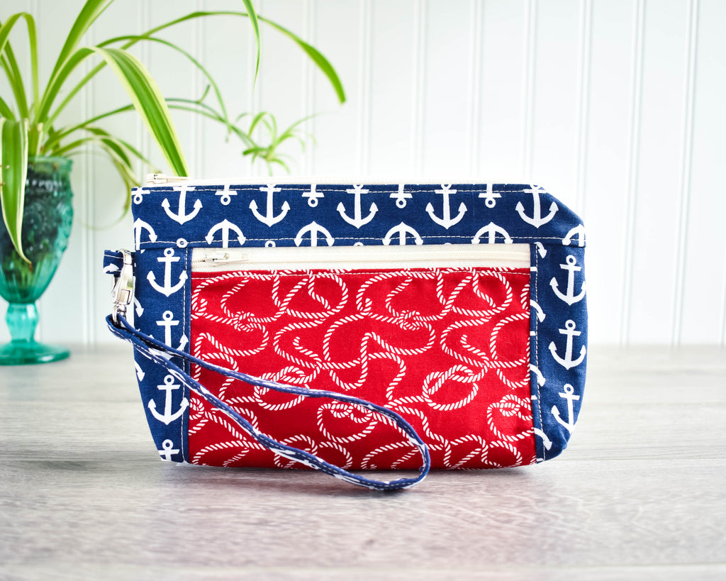 Zipped wristlet standing on wooden floor with green plant in the background